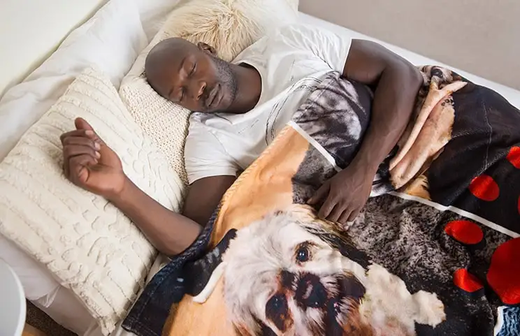 Een man slaapt op het bed onder een aangepaste Printerpix deken met hondenontwerp.