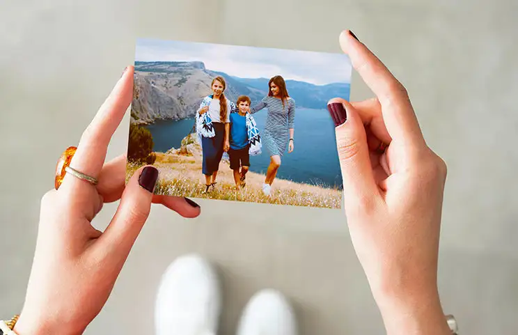 Handen die een fotoafdruk vasthouden van drie kinderen op vakantie